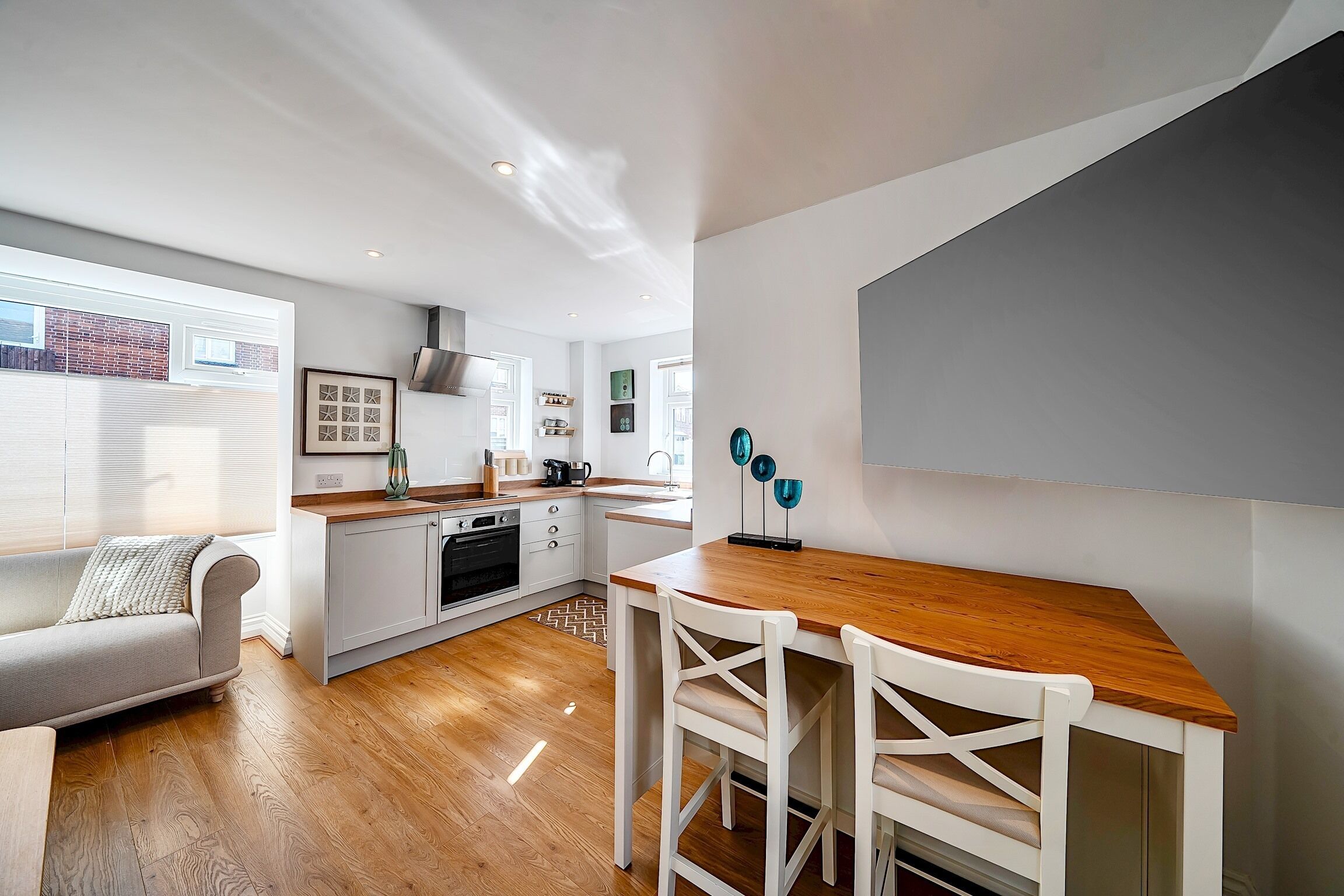 Een moderne keuken met een houten aanrecht, witte kasten en een eethoek met witte stoelen.