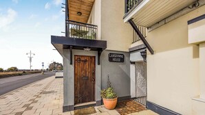 Un edificio con una porta in legno, un cartello con la scritta 'Lansdowne House', una pianta in vaso e un ingresso piastrellato.