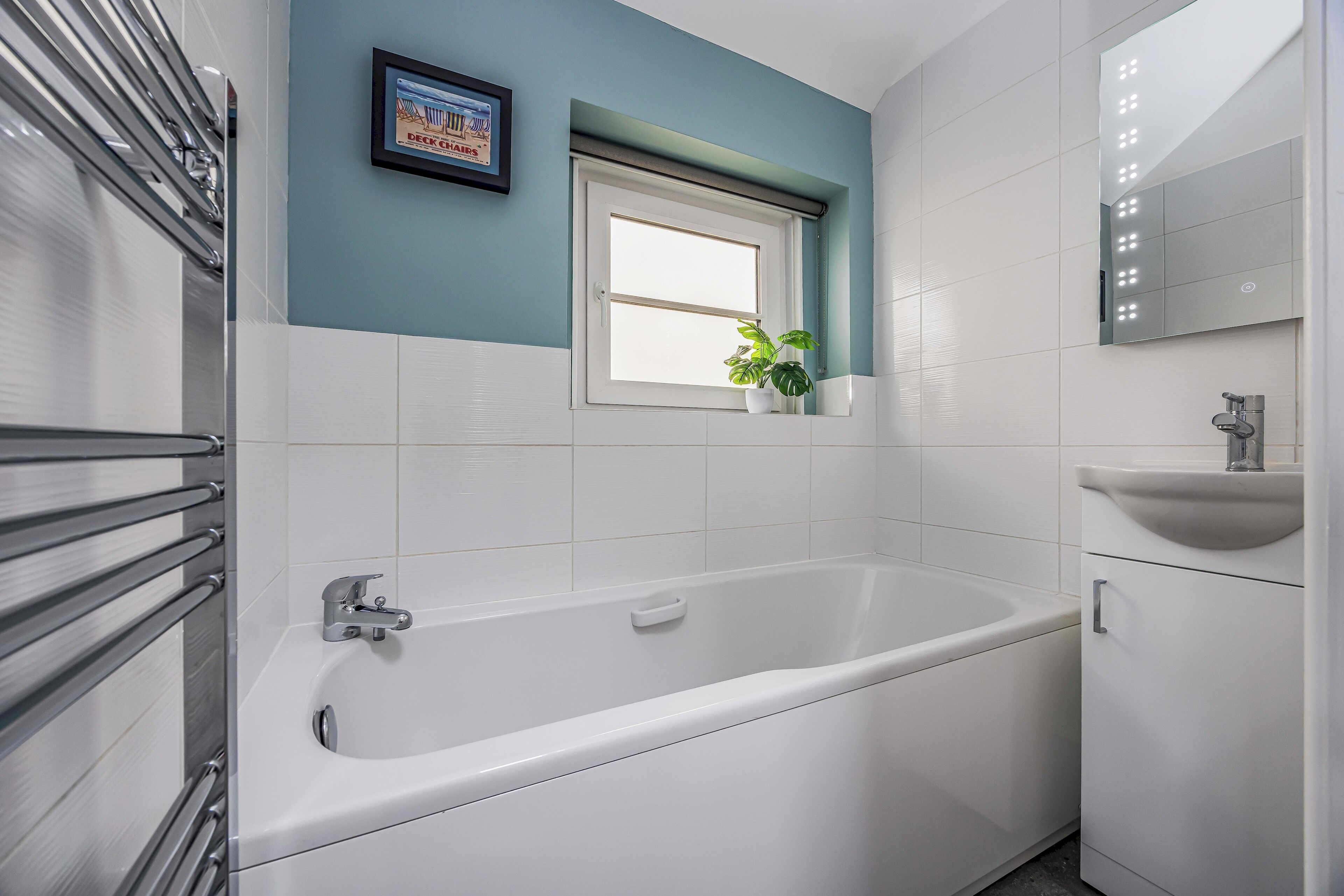 A modern bathroom with a bathtub, a window, a sink, and a potted plant.