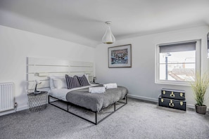 A bedroom with a bed, bedside table, lamp, picture, window, and storage boxes.