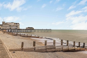A beach with a wooden walkway leading to a pier, a building with a balcony, and a clear sky.