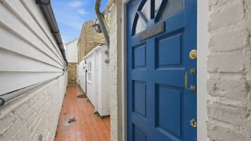 A narrow alleyway with a blue door labeled 'The Rafters' and a white brick wall.