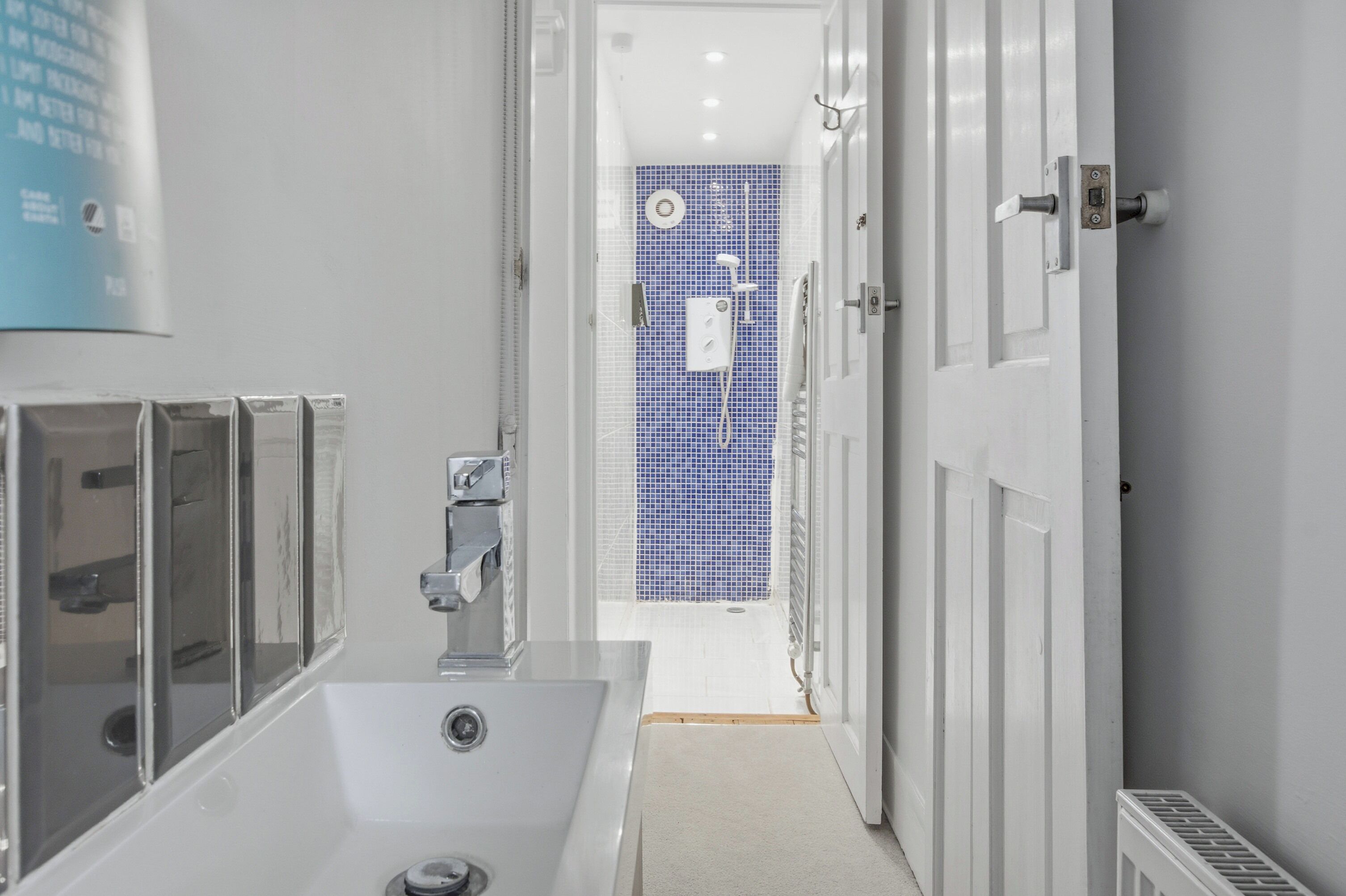 A modern bathroom with a white sink, a shower with a blue tiled wall, and a door leading to another room.