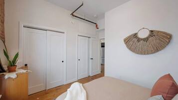 Een slaapkamer met een bed, een wandventilator, een kamerplant en een houten dressoir.