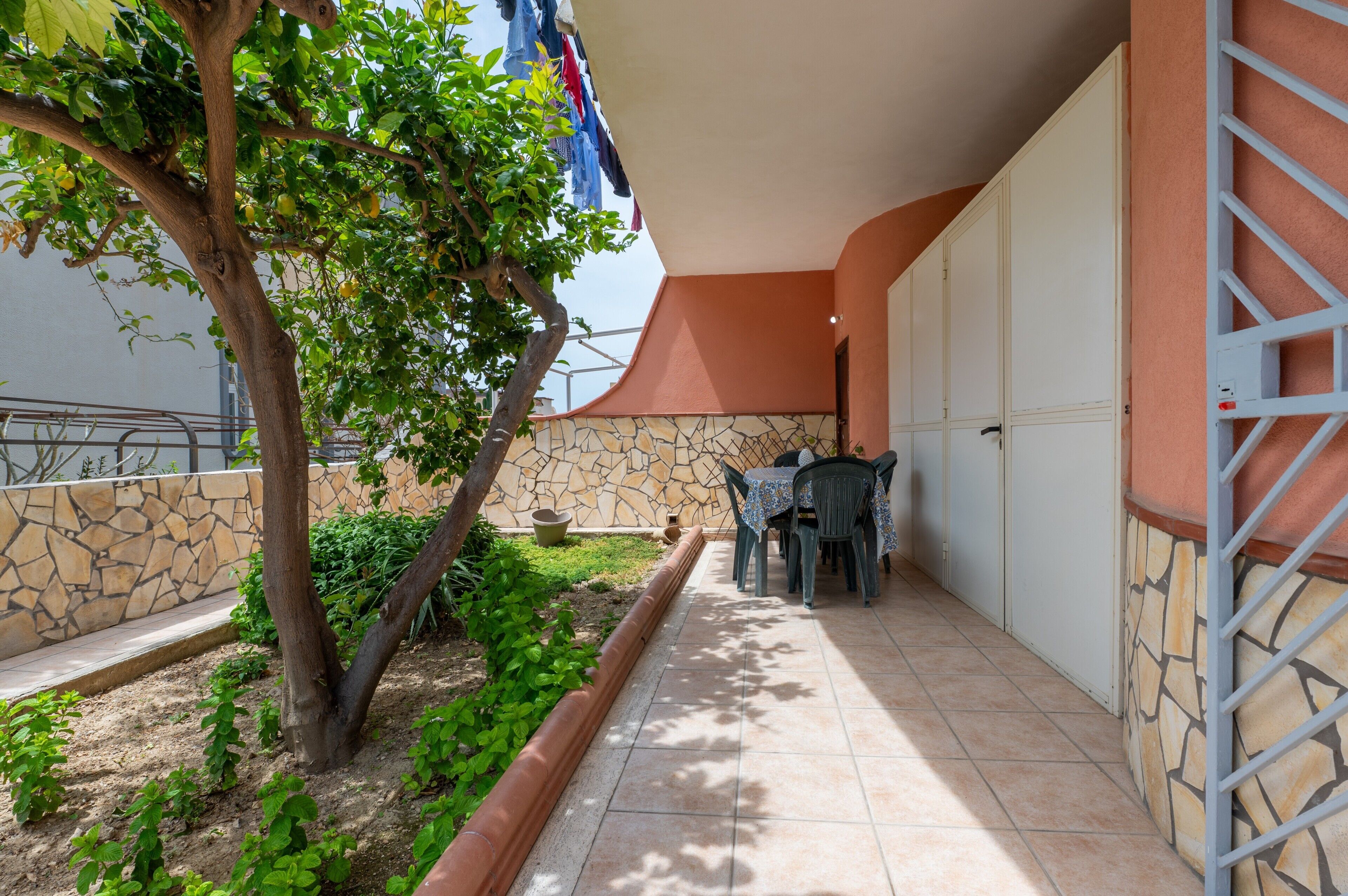 Une terrasse avec une table et des chaises, un arbre et un mur en pierre.