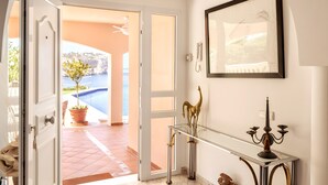 Una puerta abierta que da a un área junto a la piscina, con una planta en maceta, un candelabro y un cuadro en la pared.