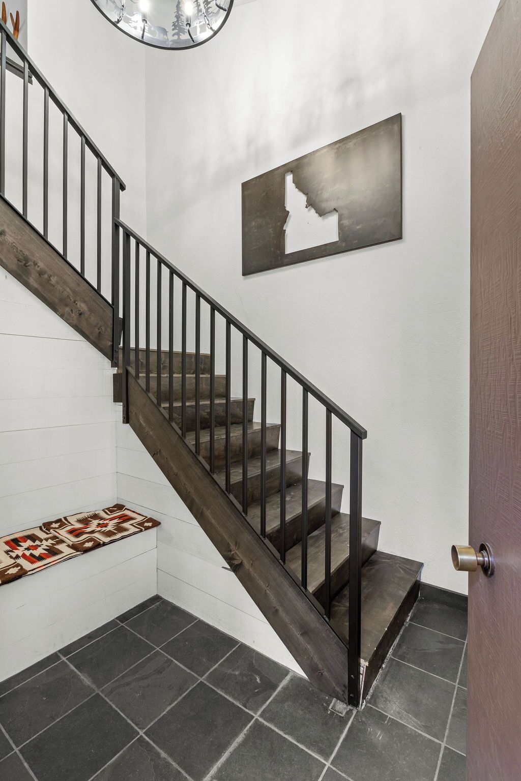 A staircase with a wooden handrail and dark steps, leading to a landing with a patterned rug.