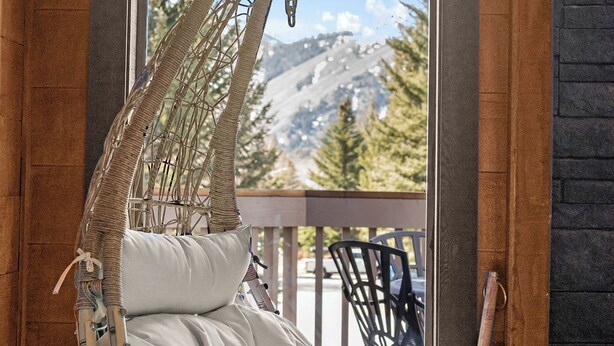 Ein hängender Korbstuhl mit Kissen, eine Holzschrank und ein Blick auf eine Berglandschaft durch ein Fenster.