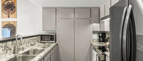 A compact kitchen with a granite countertop, stainless steel appliances, and a microwave.