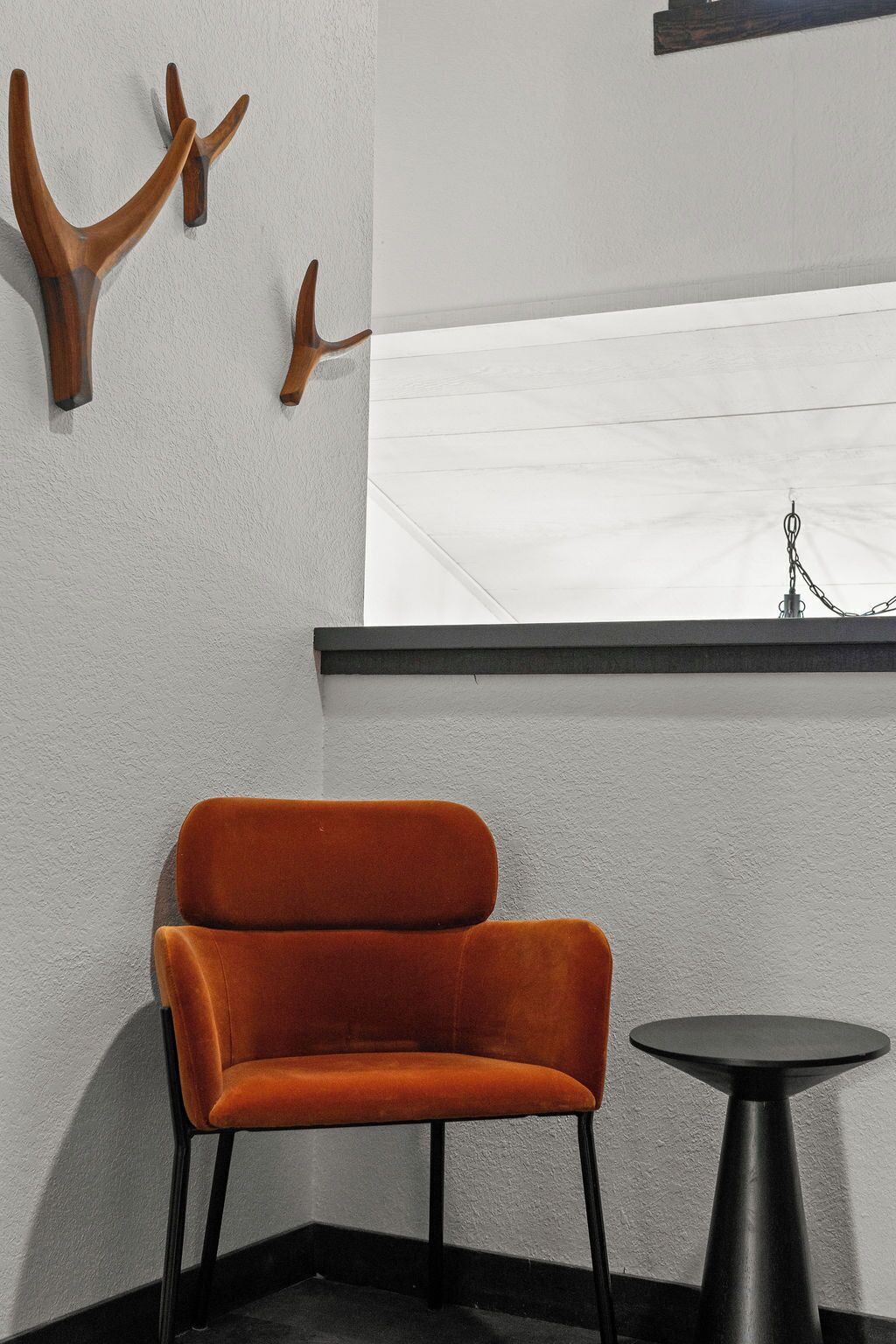 Una habitación con una única silla naranja, una pequeña mesa redonda y dos adornos de asta de madera en la pared.