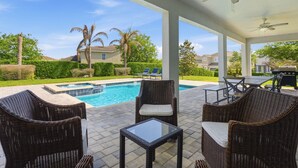 Um alpendre coberto com móveis de vime, piscina e vista para o bairro.