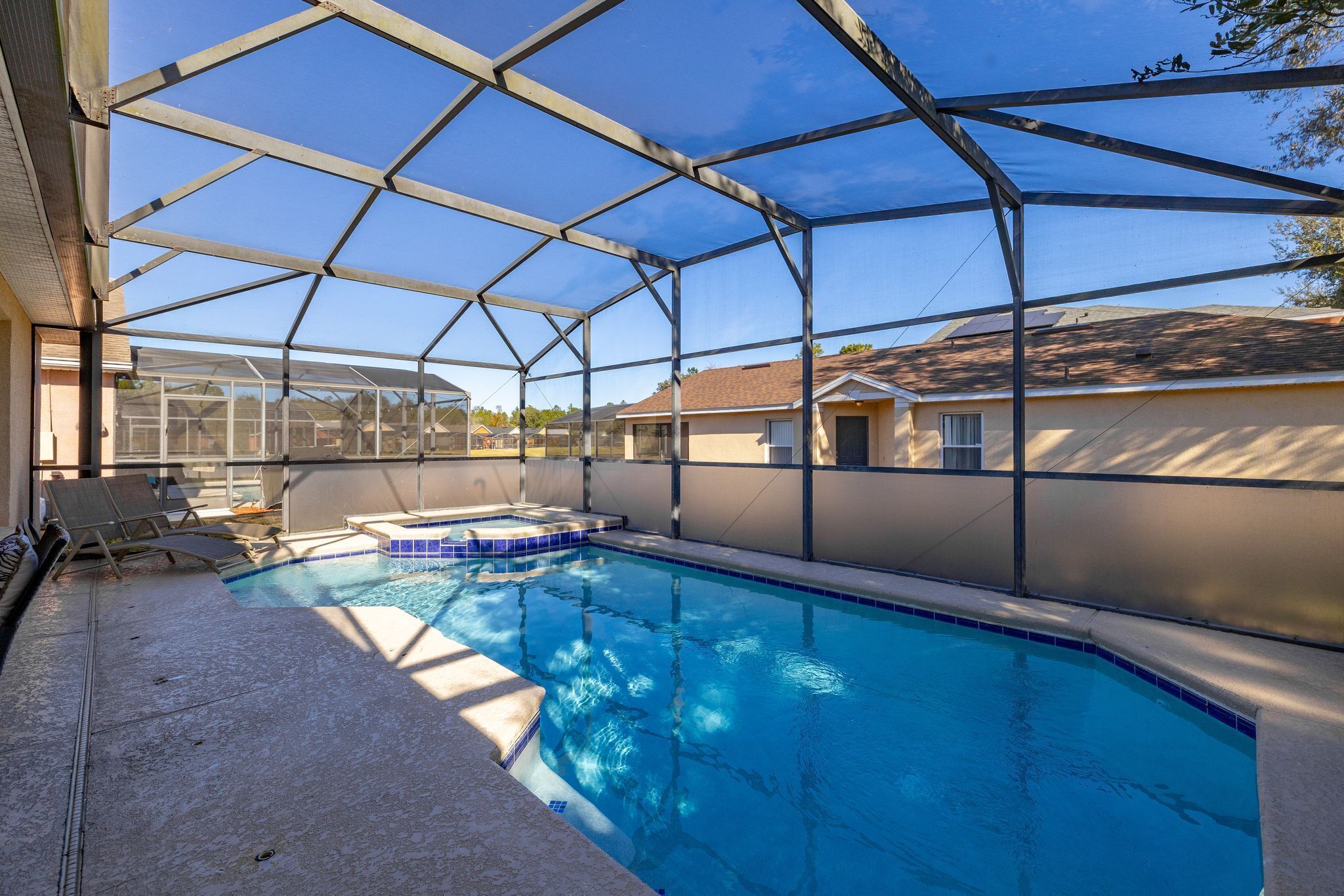 Une piscine couverte avec une structure en verre, un jacuzzi et des chaises longues.
