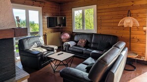 A cozy living room with wooden walls, a leather sofa, a coffee table, and a television. - T3 fully equipped - short stay / mobility lease - balcony overlooking the vineyards (Prignac-et-Marcamps)