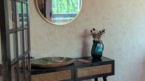 A room with a round mirror on the wall, a small table with a vase, and a door with a metal grille. - T3 fully equipped - short stay / mobility lease - balcony overlooking the vineyards (Prignac-et-Marcamps)