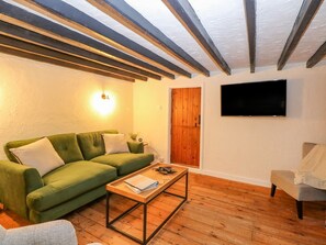 A living room with a green sofa, a wooden coffee table, a television mounted on the wall, and a wooden door. - Vintner's Cottage (Norwich)