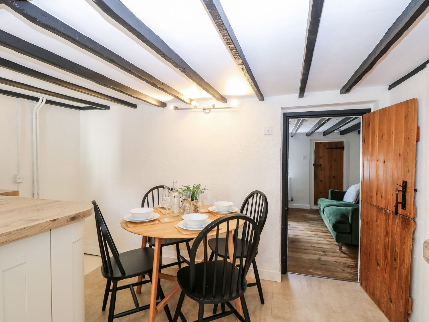Een eethoek met een houten tafel en zwarte stoelen, een keuken met witte kasten en een houten deur die leidt naar een andere kamer.