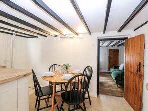 A dining area with a wooden table and black chairs, a kitchen with white cabinets, and a wooden door leading to another room. - Vintner's Cottage (Norwich)