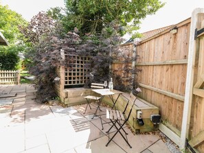 A patio with a wooden table and chairs, a wooden fence, and a lattice structure with plants. - Vintner's Cottage (Norwich)