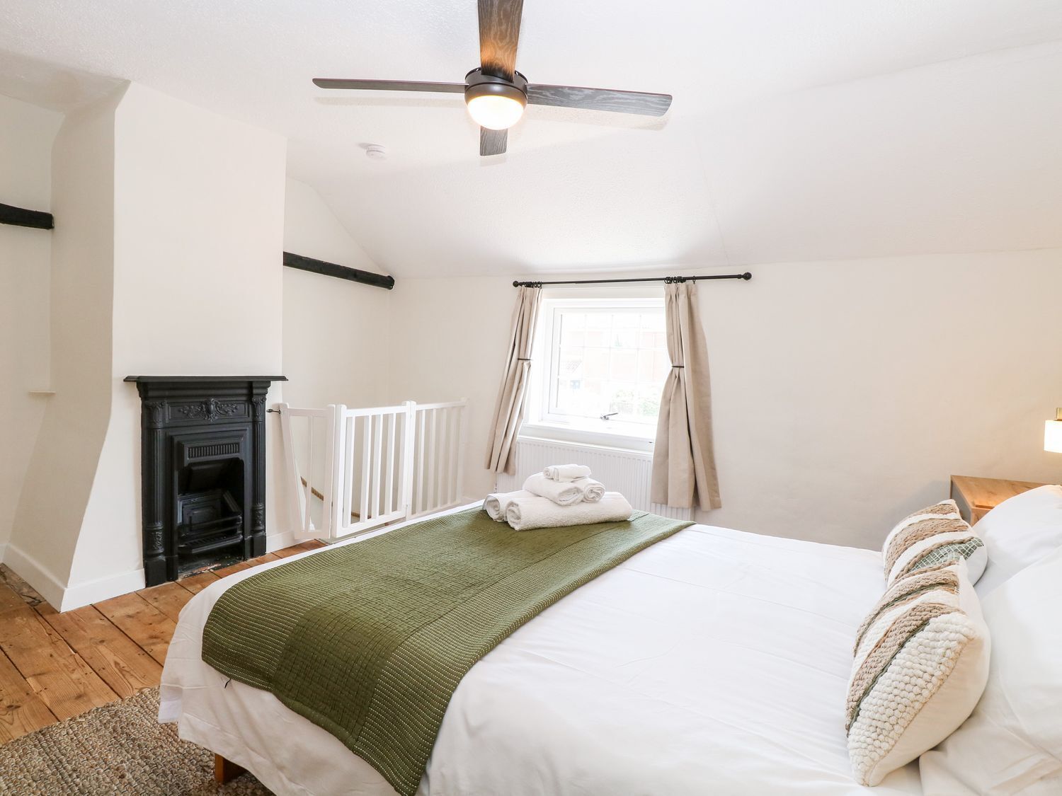 Een slaapkamer met een bed, een plafondventilator, een open haard en een raam met gordijnen.
