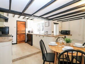 A kitchen with a wooden door, a sink, a microwave, and a dining area with a table set for four. - Vintner's Cottage (Norwich)