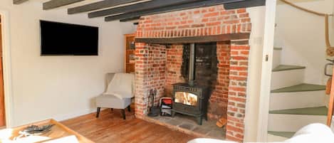 Una habitación acogedora con chimenea de ladrillo, un sillón cómodo, una mesa de madera y una escalera.
