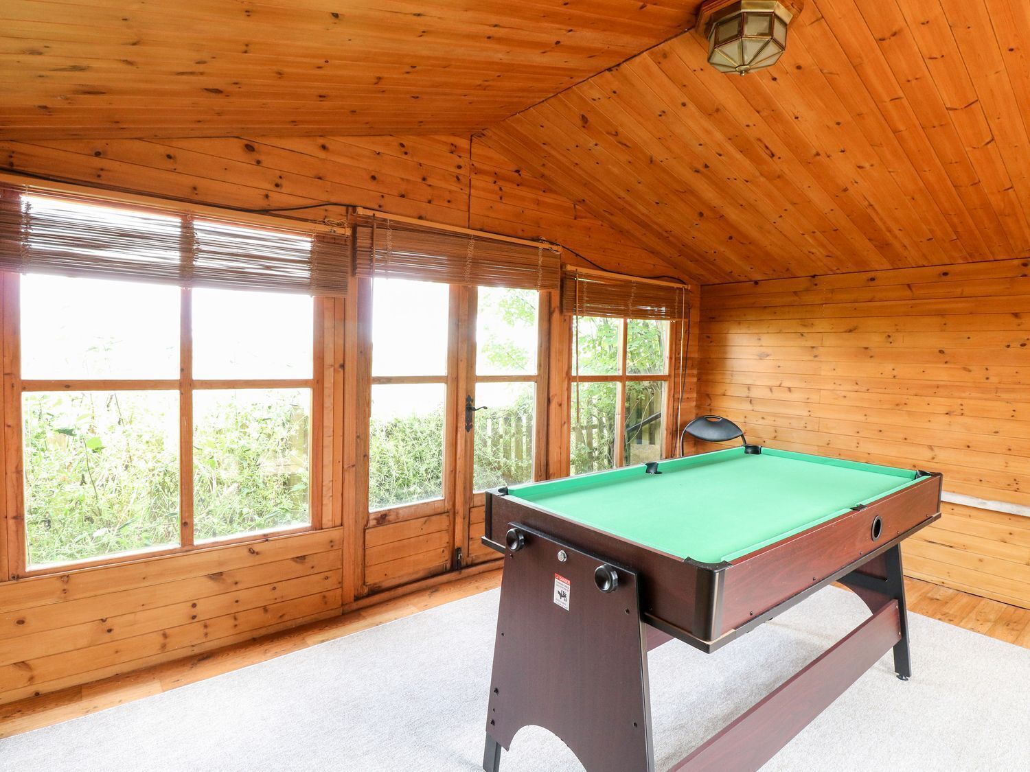 A pool table in a room with wooden walls and large windows.