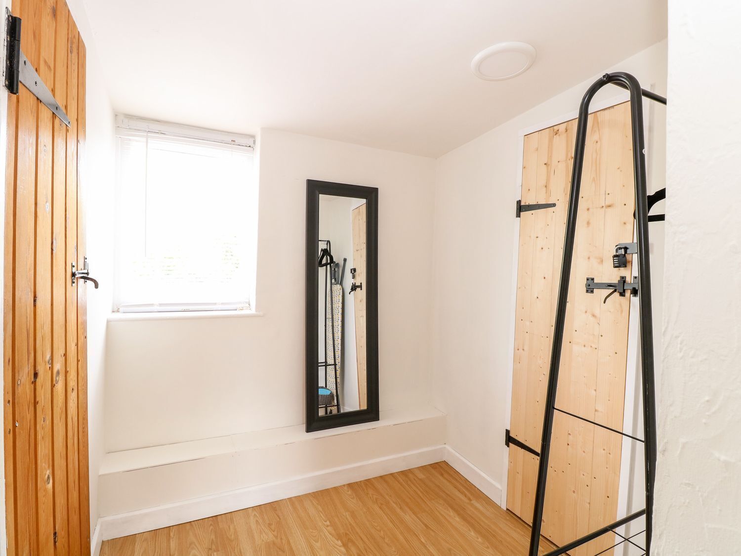 Une pièce avec un plancher en bois, une fenêtre avec des stores, un miroir et une échelle en métal.
