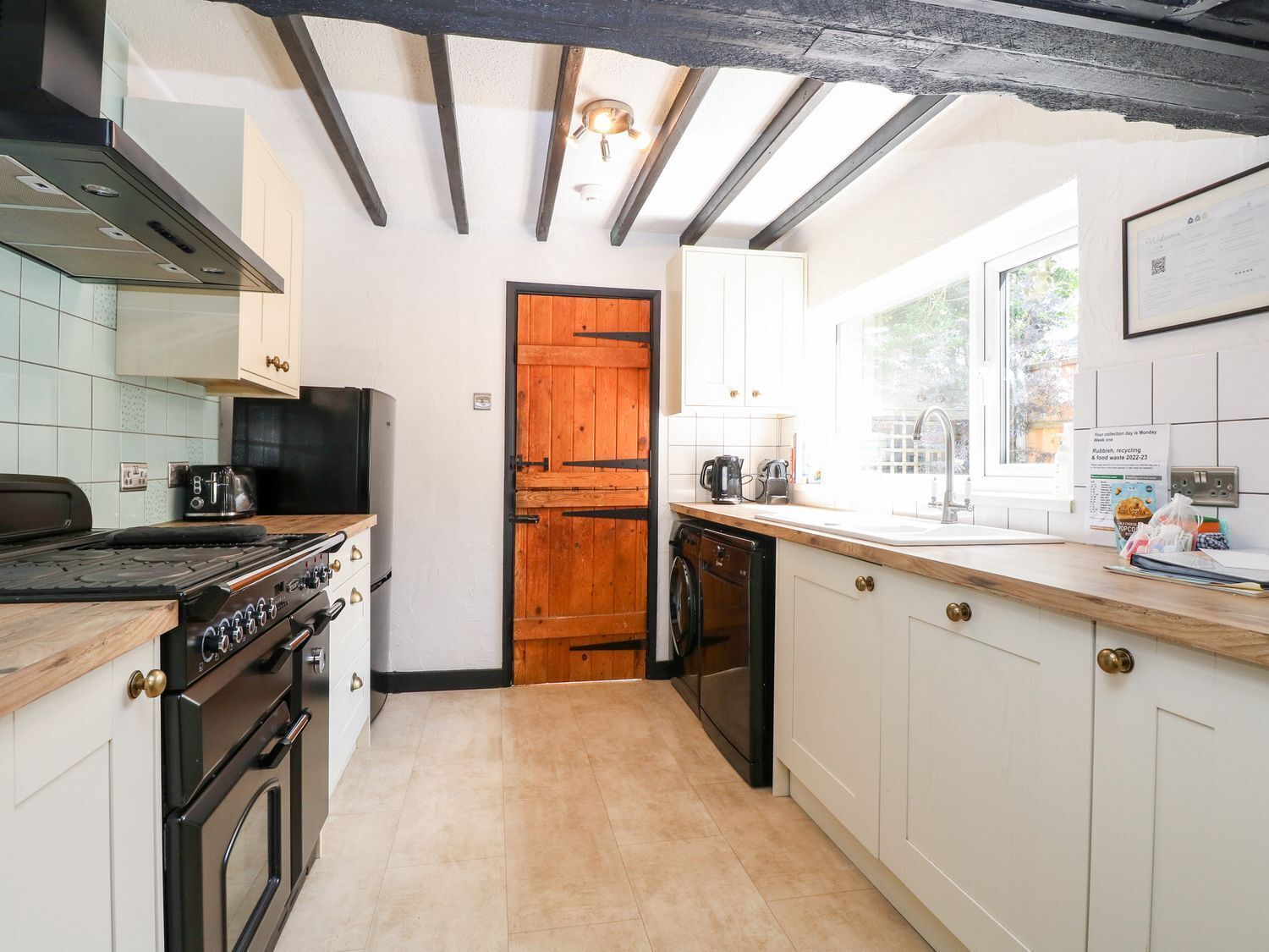 Una cocina con puerta de madera, estufa, lavavajillas y ventana con vistas.