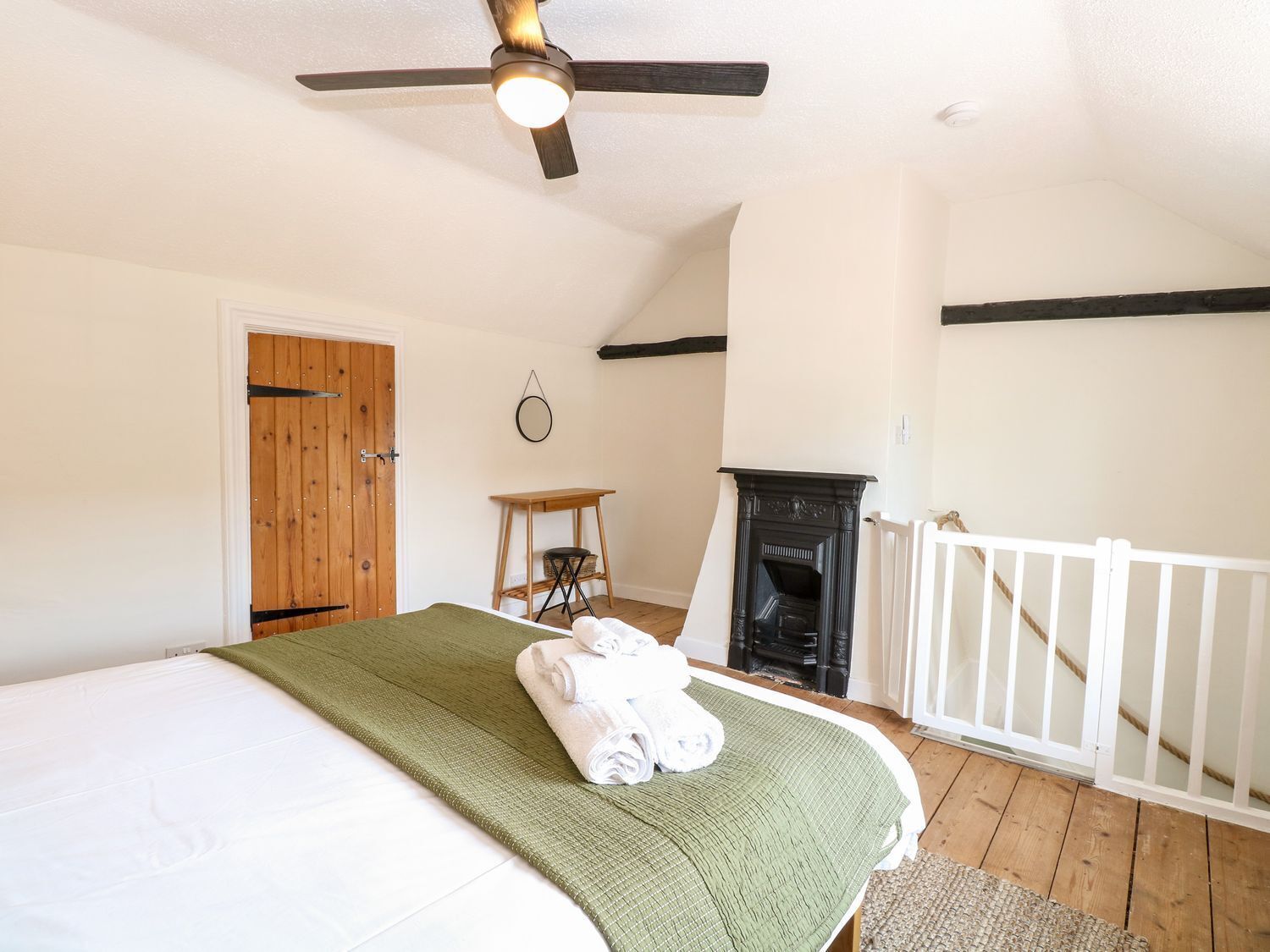 A bedroom with a bed, a wooden door, a fireplace, a white railing, and a ceiling fan.