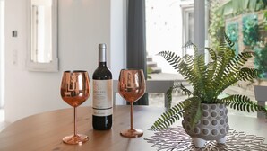A table with a wine bottle and two glasses, a potted fern, and a window with a view of greenery. - Vacation Home 'Casa Dell Anna' with Sea View, Wi-Fi and Air Conditioning (Icod de los Vinos)