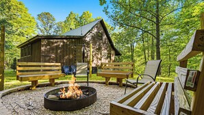 A rustic cabin with a fire pit, wooden benches, and a clear view of the surrounding forest. - Cozy* Secluded*Firepit*Hot Tub*Seeps 7 (Pigeon Forge)