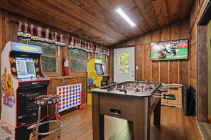 Ein Zimmer mit Holzboden, einem Kicker, einem Fernseher und zwei Spielautomaten.