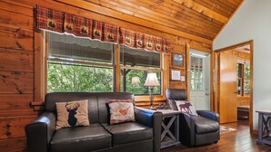 A log cabin interior with a leather sofa, a wooden table, and a door leading to another room. - Cozy* Secluded*Firepit*Hot Tub*Seeps 7 (Pigeon Forge)