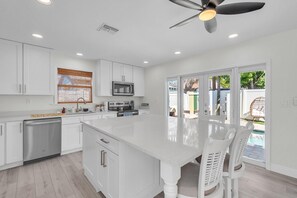 A modern kitchen with white cabinetry, a central island, and a ceiling fan. - Sunny Palms (Treasure Island)