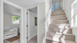Eine Treppe führt zu einer zweiten Etage, einem Schlafzimmer mit Bett und Fenster sowie einer Tür zu einem weiteren Raum.