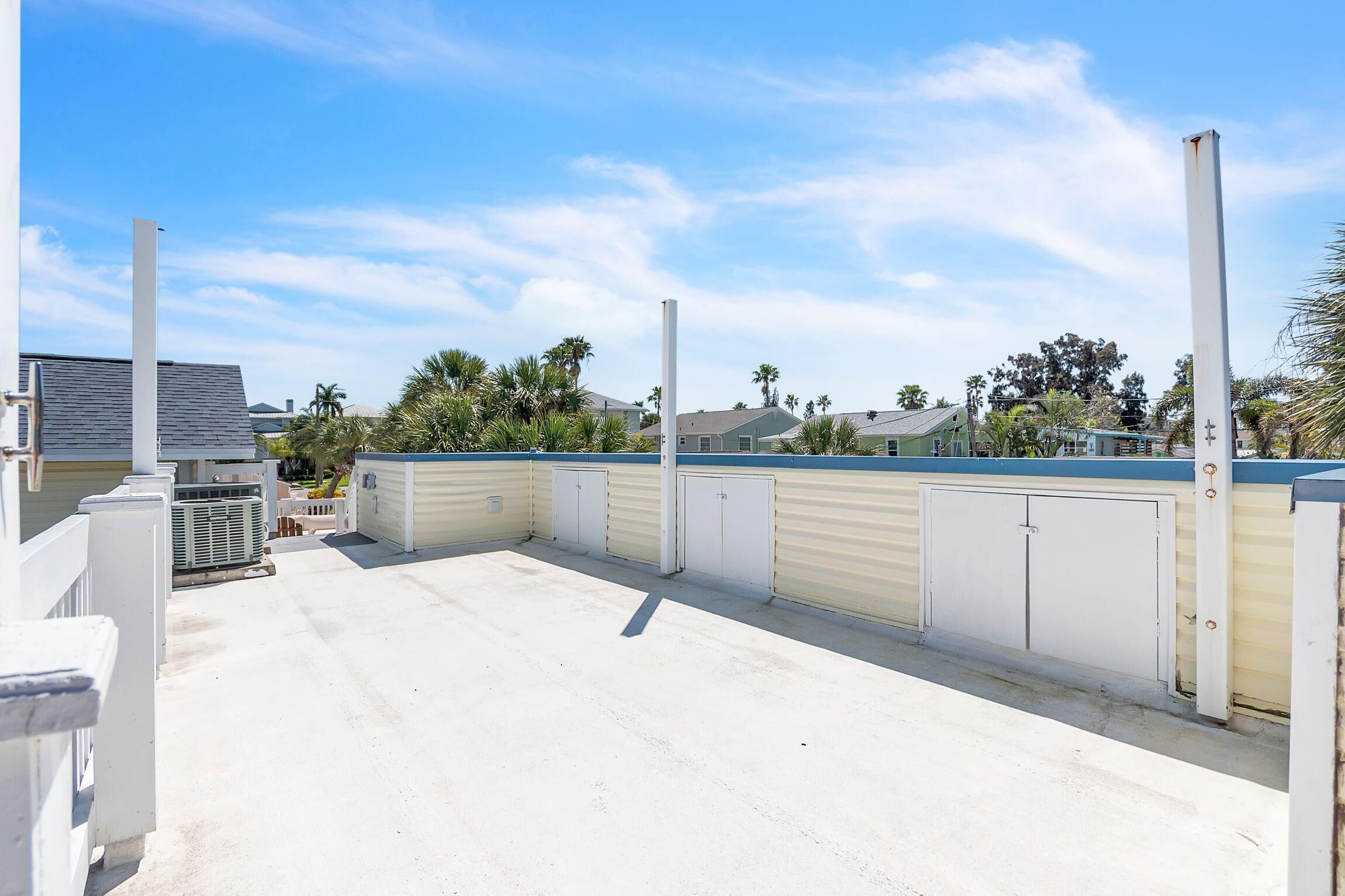 A rooftop terrace with a concrete floor, metal railings, and a view of residential buildings and palm trees.