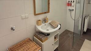 A modern bathroom with a white sink, a mirror, a glass shower enclosure, and a wicker basket. - Stylish apartment in the city center (Graz)
