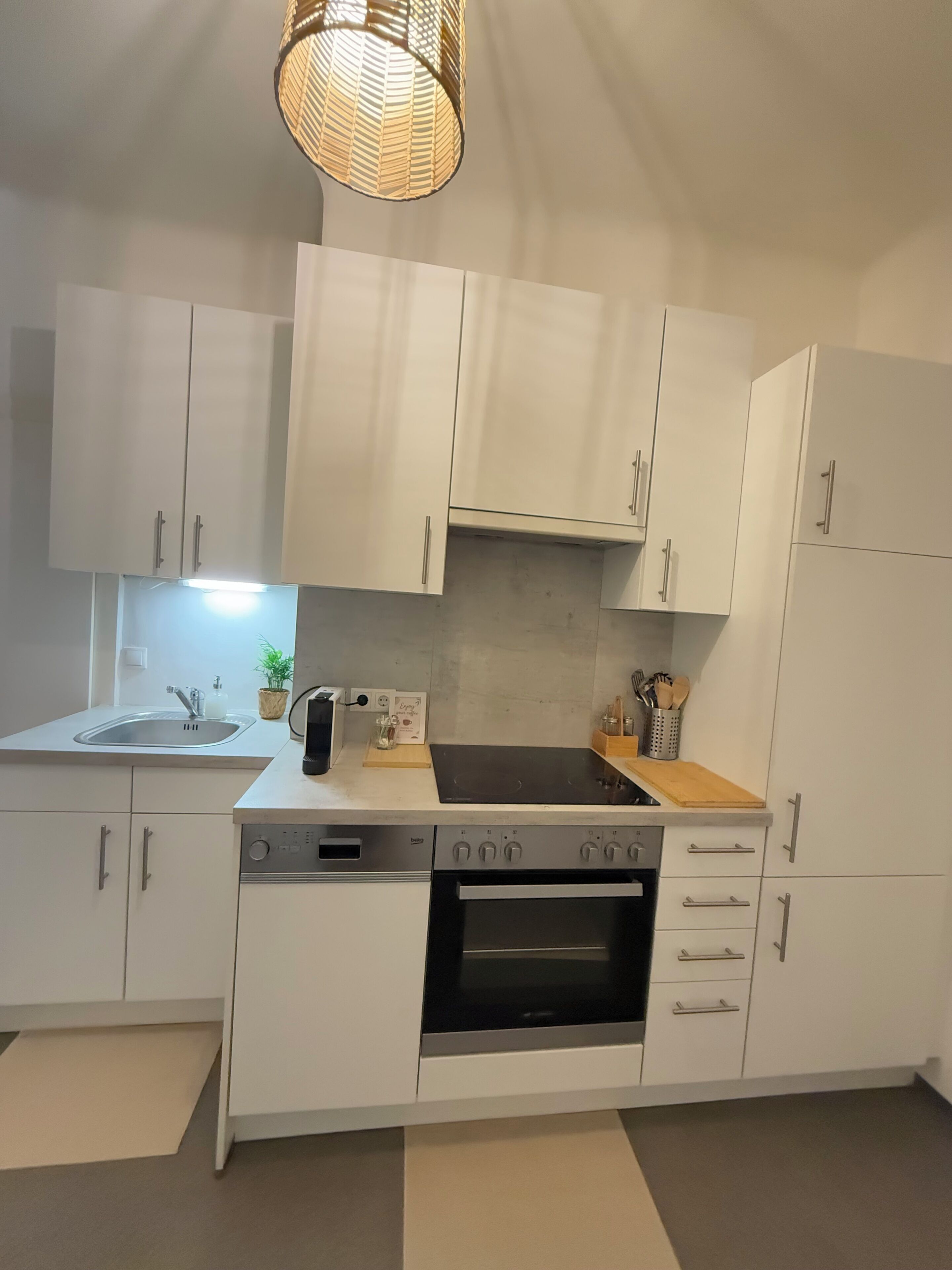 A modern kitchen with white cabinets, a built-in oven, a dishwasher, and a sink.