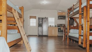 A bunk bed room with a kitchen area, including a refrigerator, microwave, and stove.