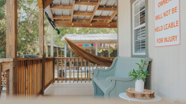 A covered porch with a hammock, a light blue bench, and a sign stating 'OWNERS WILL NOT BE HELD LIABLE FOR INJURY.'