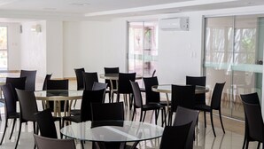 Un espace repas moderne avec des tables en verre et des chaises noires, une cloison en verre et un appareil de climatisation fixé au mur.
