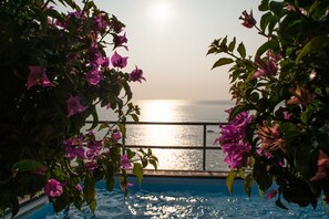 A pool with a view of the sea, surrounded by pink flowers.