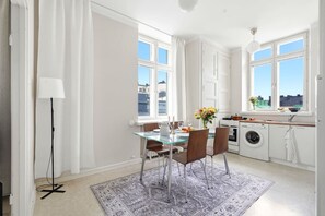A modern kitchen with a washing machine, a dining area with a glass table, and large windows. - Balcony Studio | Rooftop Views | Tram 200m | Lift (Helsinki)