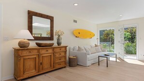 Een kamer met een houten kast, een witte bank, een tafel, een lamp, een spiegel en een surfboard.