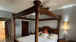 Een hemelbed met een houten hoofdbord, een nachtkastje en een wandlamp.