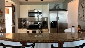 Een moderne keuken met roestvrijstalen apparatuur, granieten aanrechtbladen en een centraal eiland met stoelen.