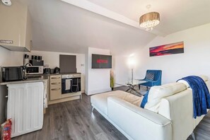Un espace de vie moderne comprenant un coin cuisine, un téléviseur à écran plat, un canapé et un tableau au mur.