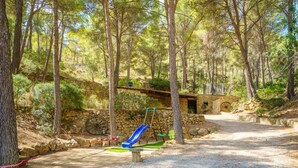 A forested area with a gravel path, a stone wall, a wooden structure, and a blue slide. - Holiday Home 'Can Miquel De Sa Teia' with Mountain View, Private Pool and Wi-Fi (Illes Balears)