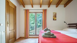 A bedroom with a bed, a wooden door, a window with curtains, and a view of trees. - Holiday Home 'Can Miquel De Sa Teia' with Mountain View, Private Pool and Wi-Fi (Illes Balears)