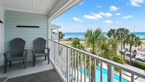 Een balkon met twee Adirondack stoelen, een zwembad en uitzicht op strand en zee.
